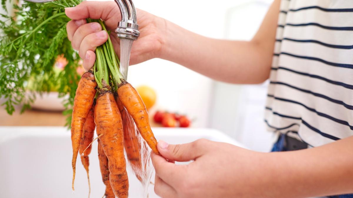 Женщина моет свежею морковь