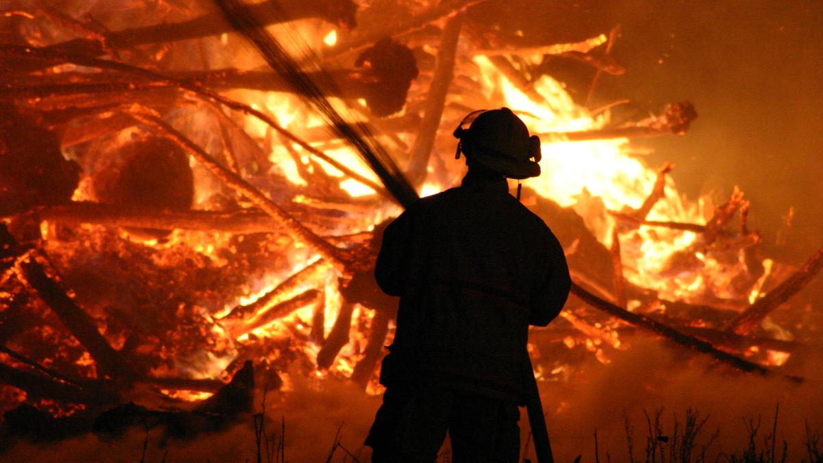 Пожарный тушит горящий дом