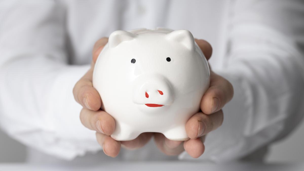 Мужчина в белой рубашке держит свинью-копилку