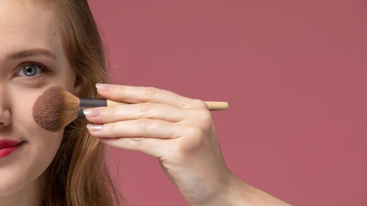 Молодая привлекательная женщина делает макияж на розовой стене