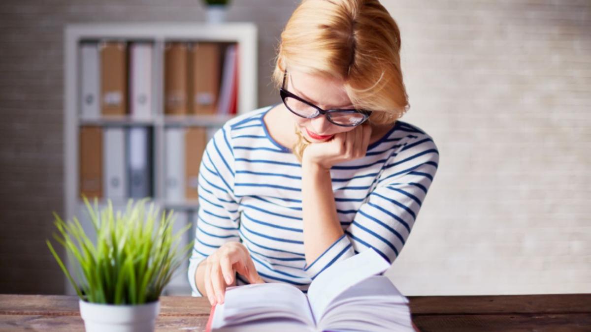 Девушка сидит за деревянным столом и читает книгу Девушка сидит за деревянным столом и читает книгу