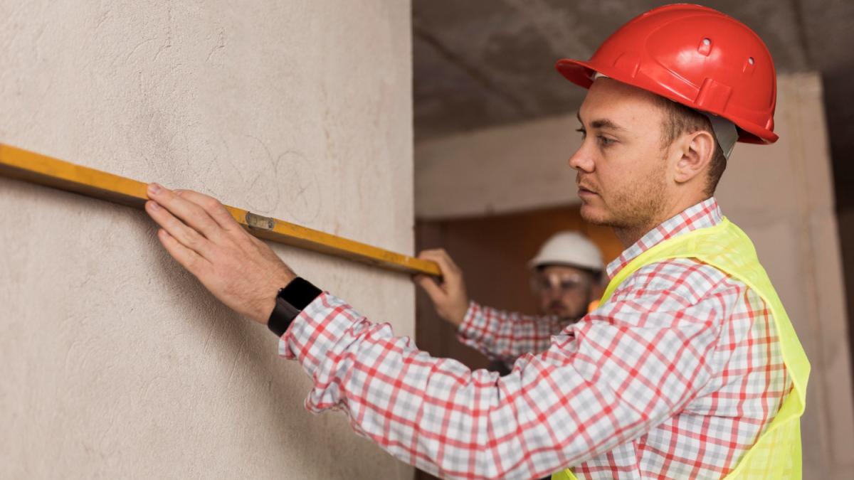 Строитель измеряет стену