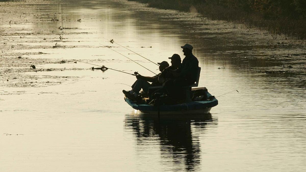 Силуэты трех мужчин на фоне зеркальной воды ловят рыбу с лодки
