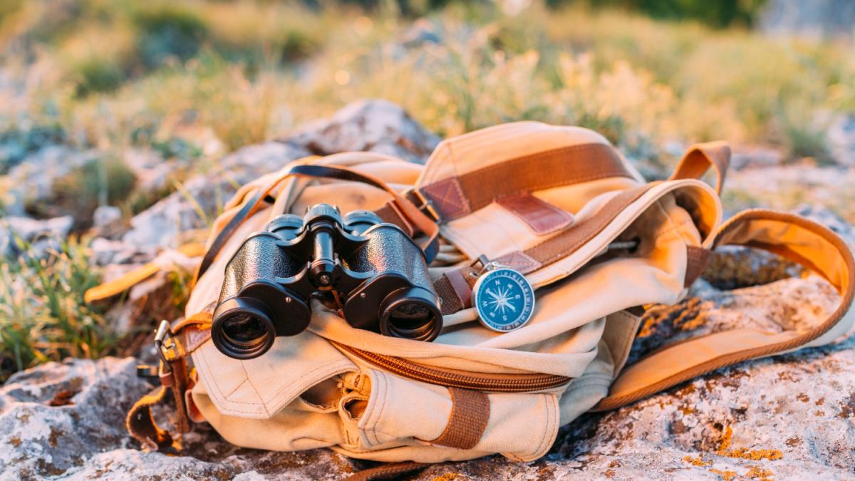 Рюкзак, бинокль и компас на камне